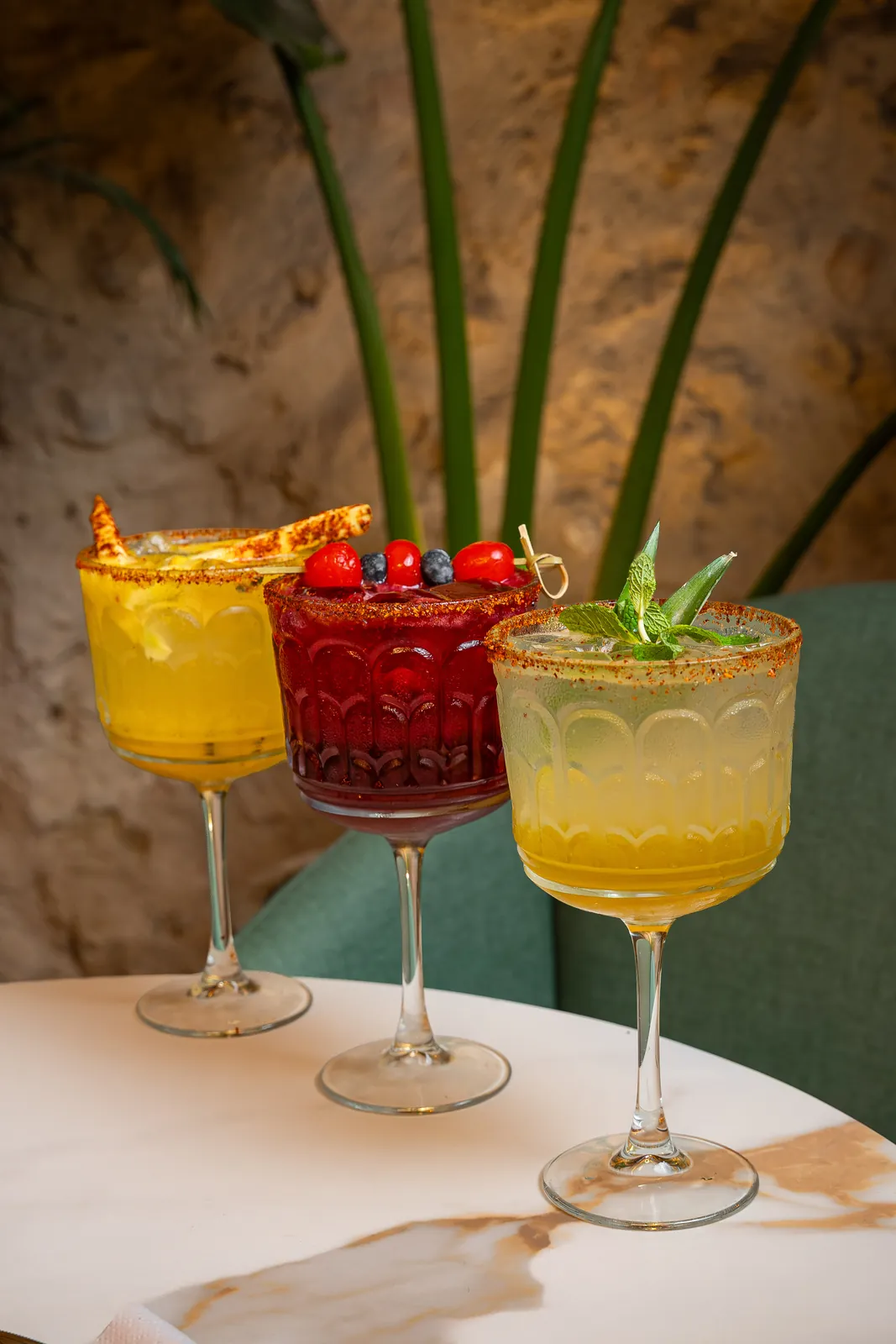 Three rimmed craft cocktails with berries and mint on a marble table